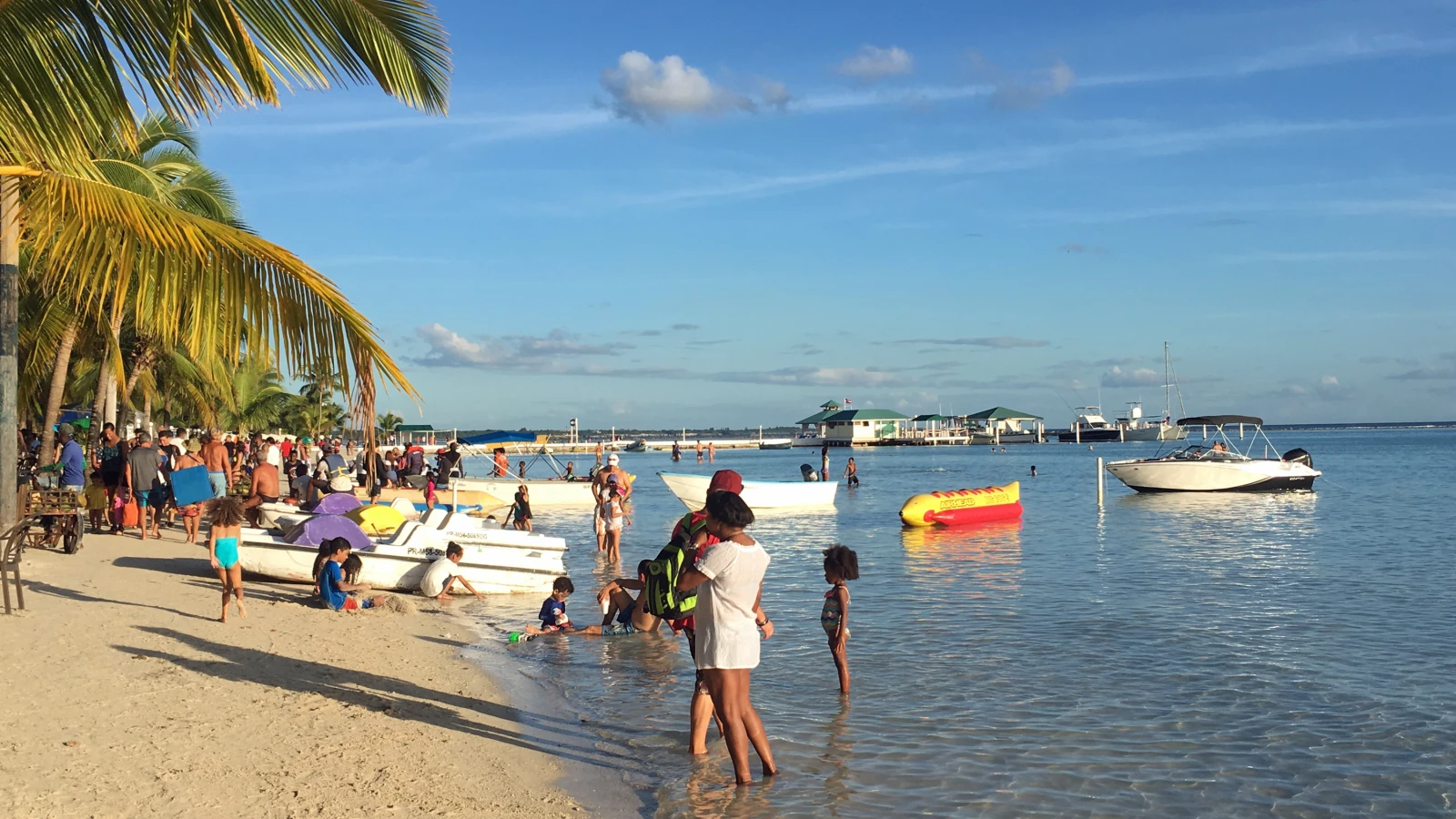 Familias en el agua bajita de la playa de Boca Chica, con botes y palmeras
