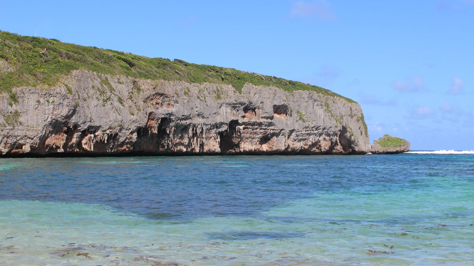 Agua clara de Playa Madama frente a un acantilado de roca con cuevas, en Las Galeras, península de Samaná