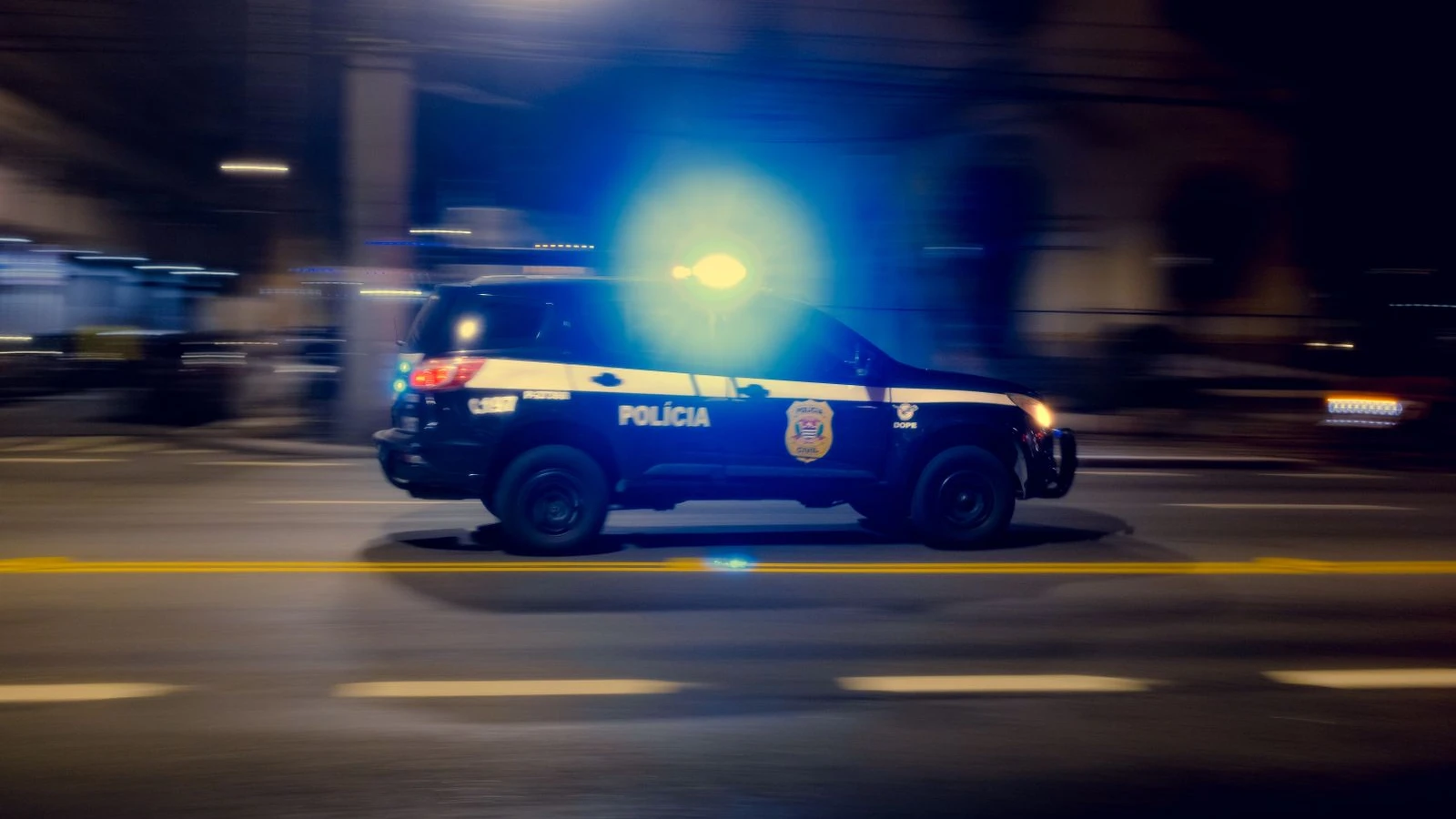 Patrulla policial con las luces encendidas manejando de noche en una avenida