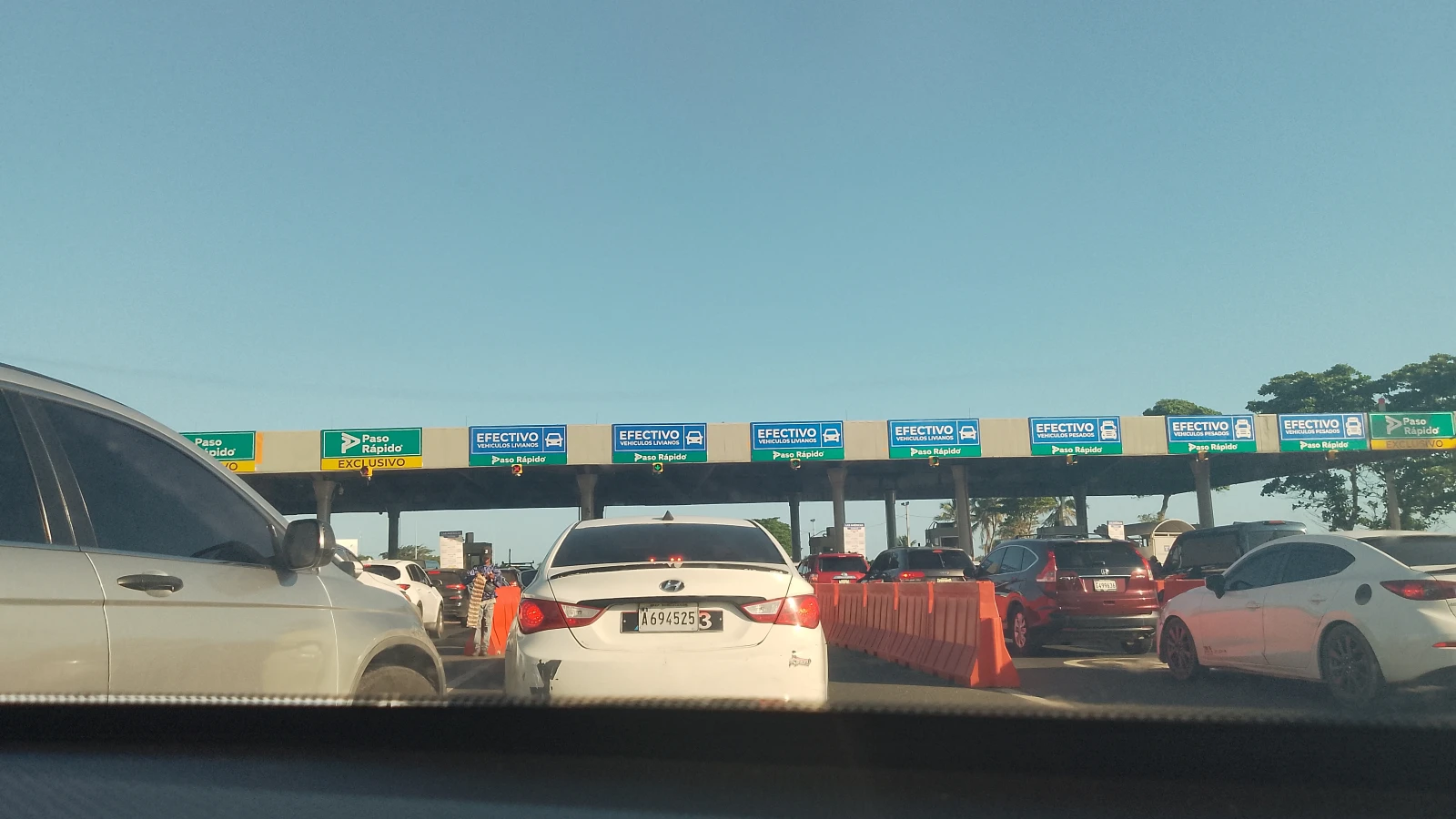 Carros haciendo fila en la estación de peaje del km 22 de la Autopista Las Américas, con carriles de efectivo y Paso Rápido