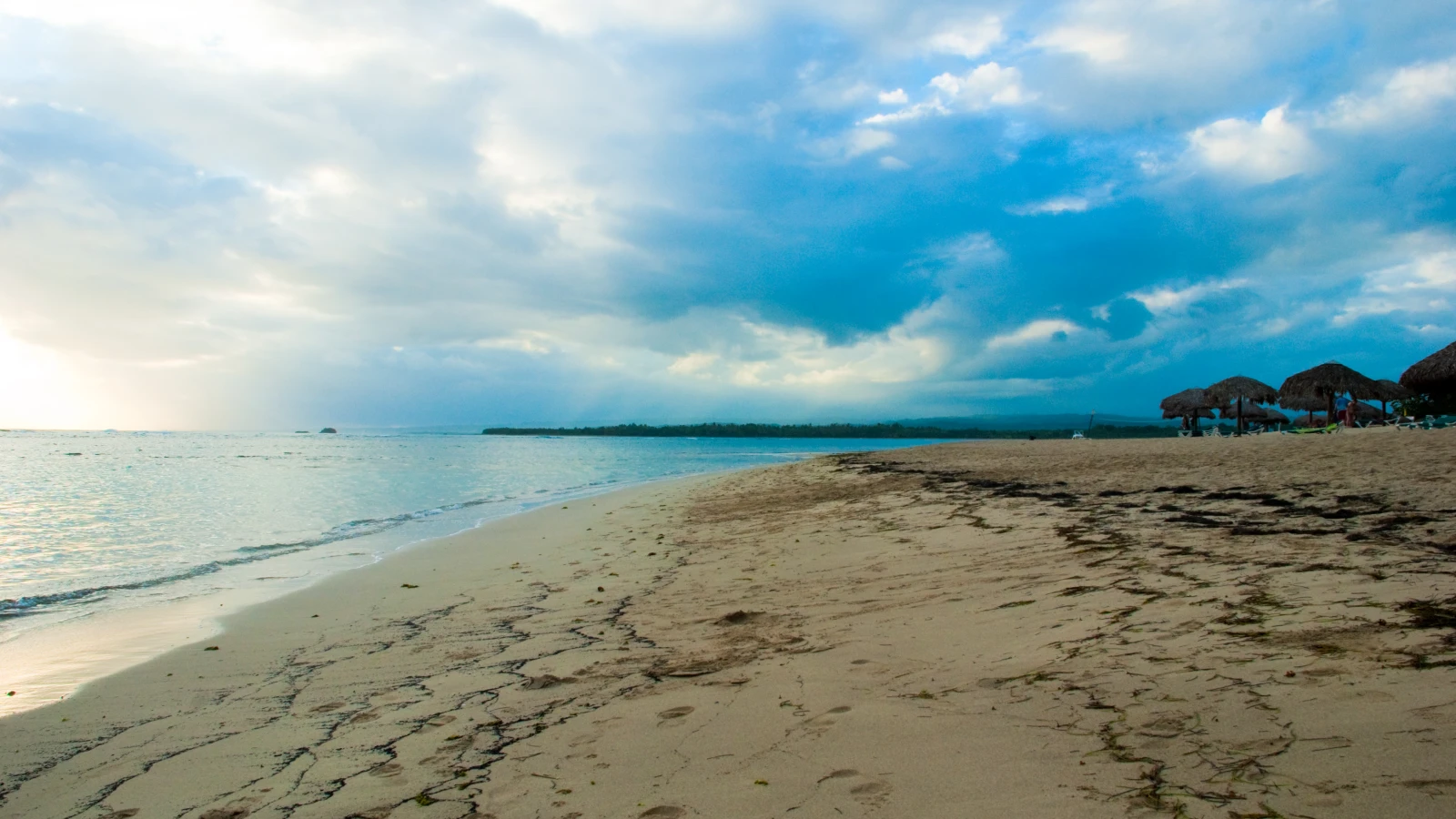 Arena y orilla de Playa Dorada en Puerto Plata al atardecer, con ranchos de paja de un hotel al fondo
