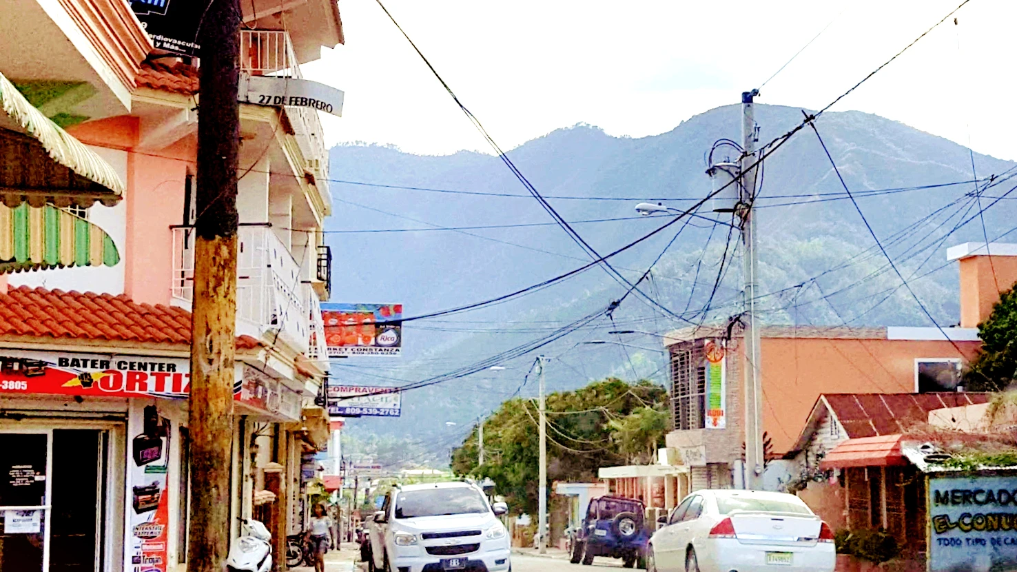 Jeepetas y un sedán en una calle de Constanza, con las montañas de la Cordillera Central al fondo
