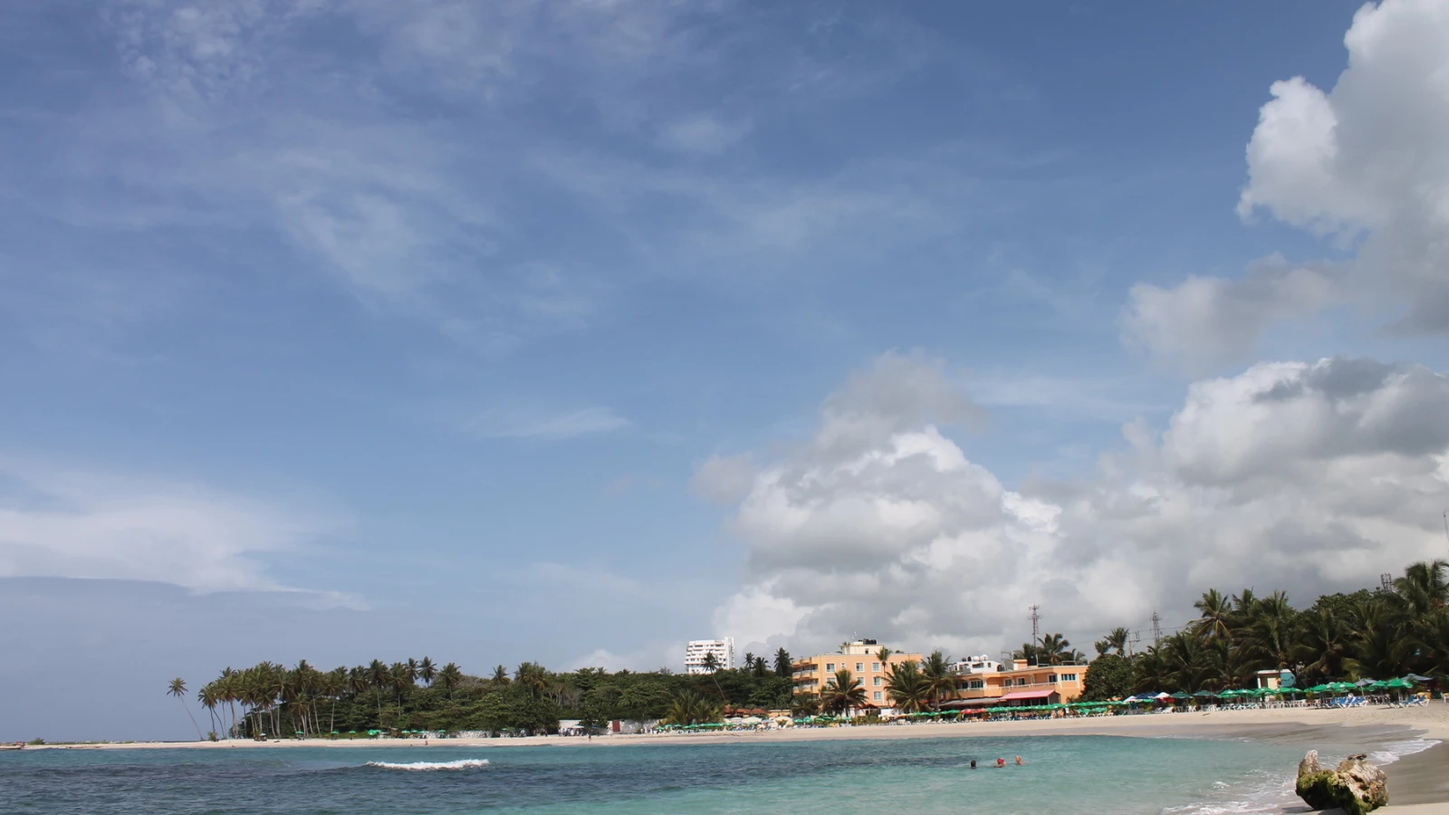 La playa pública de Juan Dolio con agua turquesa, palmeras y hoteles al fondo