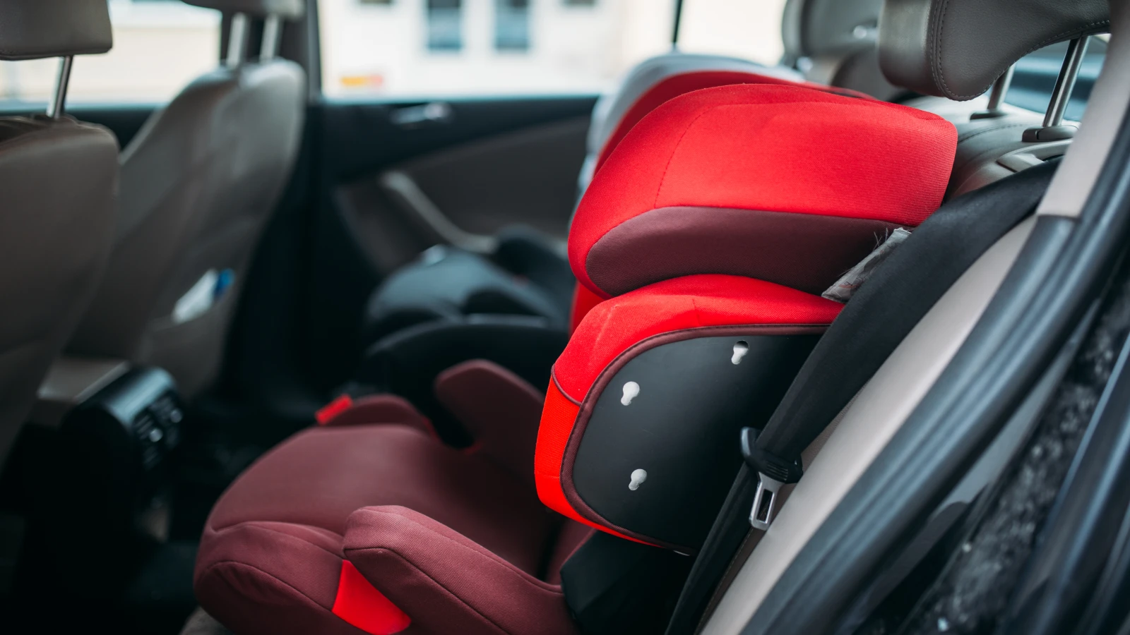 Silla elevadora roja para niño instalada en el asiento trasero de un carro